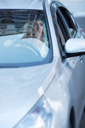 young adult blonde beautiful woman driving a car, view from behind a glassの写真素材