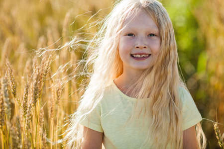 happy little blonde girl in wheat field with long hairの写真素材