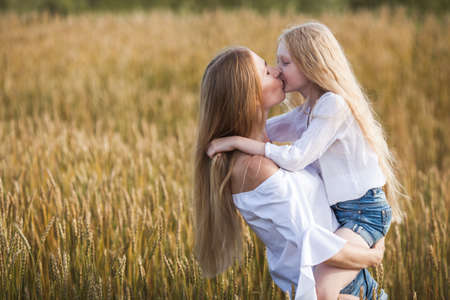 beautiful young mother kissing her daughter at the wheat field on sunsetの写真素材
