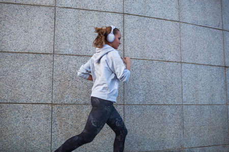 Young woman running in the city over concrete wallの写真素材