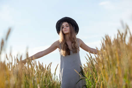 young beautiful woman wearing hat in golden wheat fieldの写真素材