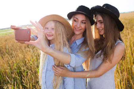 beautiful young mother and her daughters at the wheat field on a sunny day doing selfie