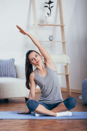 Young cheerful attractive woman practicing yoga, sitting in Sukhasana poseの写真素材