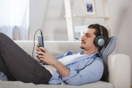 Handsome guy lying on sofa with tablet and headphonesの写真素材
