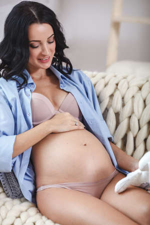 young pregnant woman with toys sitting on sofa at home