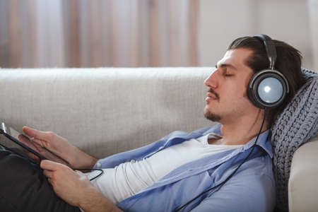 Handsome guy lying on sofa with tablet and headphonesの写真素材