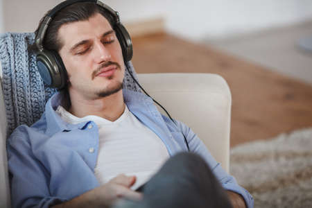 Handsome guy lying on sofa with tablet and headphonesの写真素材
