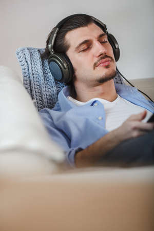 Handsome guy lying on sofa with tablet and headphonesの写真素材