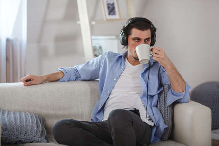 Handsome guy sitting on sofa with headphonesの写真素材