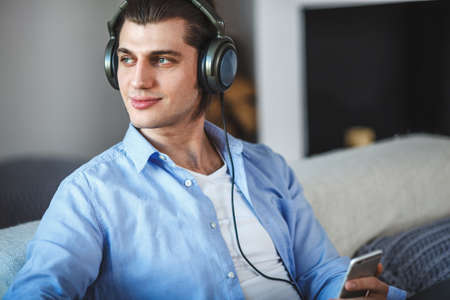 Handsome guy sitting on sofa with headphonesの写真素材