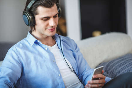 Handsome guy sitting on sofa with headphonesの写真素材