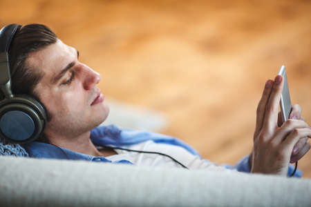 Handsome guy lying on sofa with tablet and headphonesの写真素材