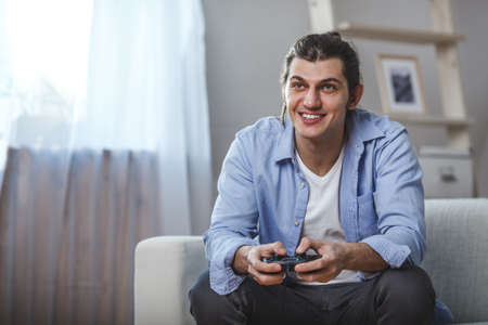 young man seated on a sofa playing video games inside his roomの写真素材