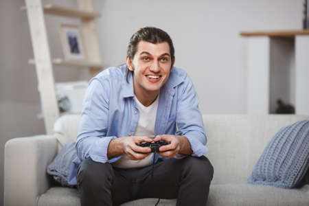 young man seated on a sofa playing video games inside his roomの写真素材