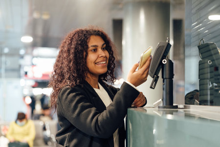 Young woman near the ticket office paying with smartphoneの写真素材