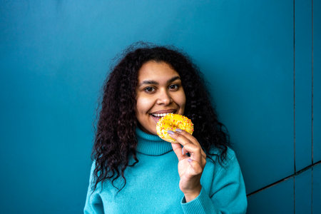 Young woman biting yellow donut near aqua wallの写真素材