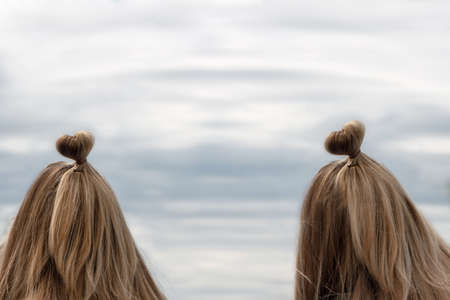 Two girls with a haircut in the form of a heart on the background of the sea, sky.の写真素材