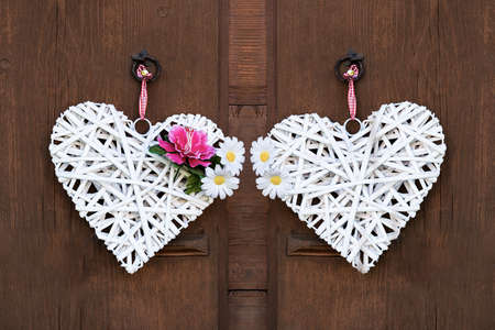 Two woven white hearts with peonies and daisies hanging on a wooden wall.の写真素材