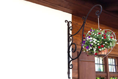 A flowerpot in the shape of a heart hangs on a forged holder on a wooden house.