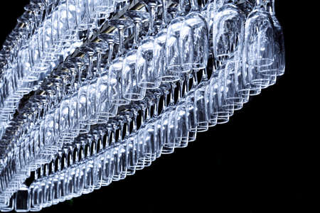 A large number of glasses in the shape of an oval hang on the holder at the bar counter on a dark background.の写真素材