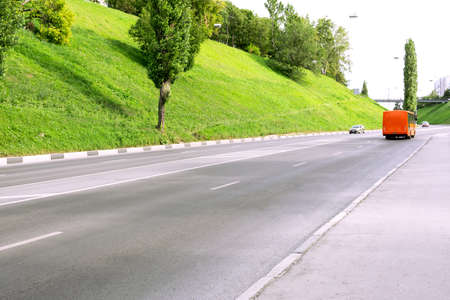 A bright orange bus is moving along a scenic road.の写真素材