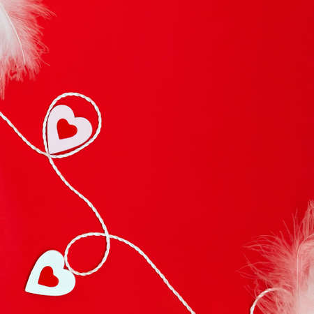 Top view of a minimalistic composition for Valentines Day on a red background with white and red hearts, feathers and a white rope. Holiday concept, greeting card, background, minimalism.の写真素材