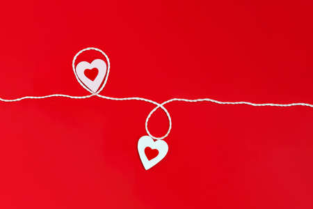 Top view of a minimalistic composition for Valentines day on a red background with white and red hearts and a white rope. Holiday concept, greeting card, background, minimalism.の写真素材