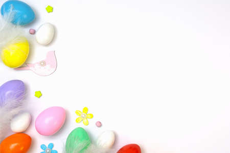Top view of an Easter composition of painted eggs in bright juicy colors on a white background with a glossy texture of white bird feathers and flowers. Holiday concept, flat layout, backgroundの写真素材