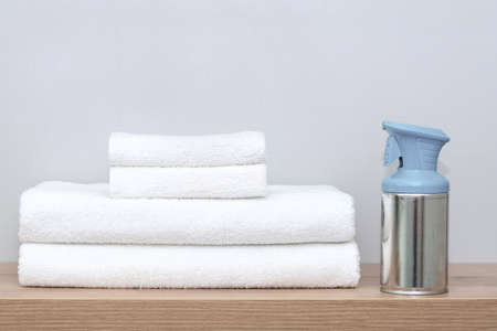 On a shelf in the bathroom are white towels of different sizes neatly folded and next to it is an air freshener. The concept of cleanliness, order and comfort in the home, textilesの写真素材