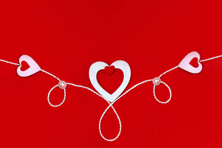 Top view of a composition for Valentine's Day on a red background with white and red hearts and a white rope. Holiday concept, greeting card, backgroundの写真素材