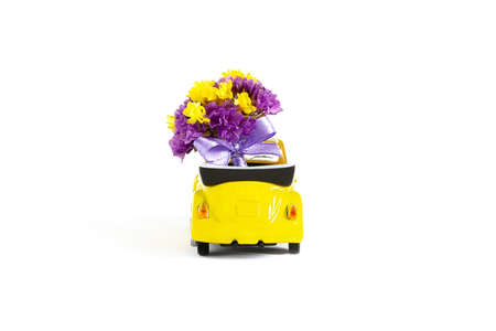 View of a colorful bouquet of purple flowers that is in a small yellow car on a white background....