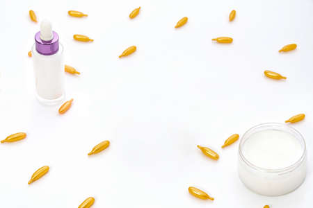 Top view of a white jar of cream, a pink pink glass bottle and golden collagen capsules on a white background. The concept of beauty, facial skin care, cosmetology, medicineの写真素材