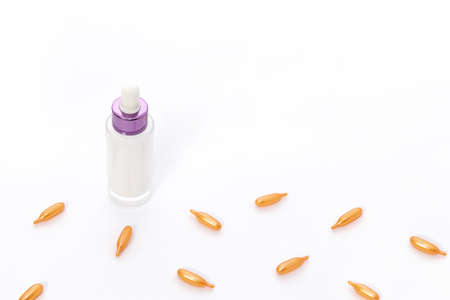 Top view on a pink pink glass bottle with white cream and orange collagen capsules on a whiteの写真素材