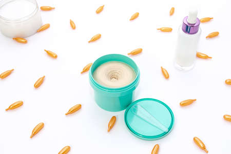 Top view on a bright turquoise jar of cream, a pink pink glass bottle and golden collagen capsules...