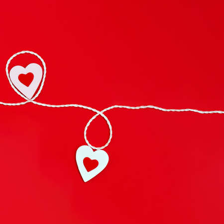 Top view of a minimalistic composition for Valentine's day on a red background with white and red hearts and a white rope. Holiday concept, greeting card, background, minimalismの写真素材