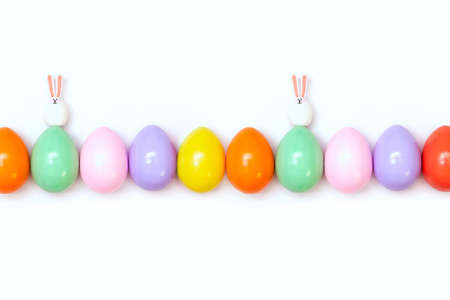 Top view of an Easter composition of painted eggs in bright juicy colors on a white background with two little rabbits. Holiday concept, flat layout, minimalismの写真素材