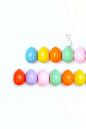 Top view of an Easter composition of painted eggs in bright juicy colors on a white background with a little rabbit. Holiday concept, flat layout, minimalismの写真素材