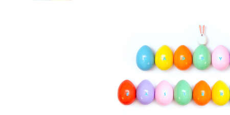 Top view of an Easter composition of painted eggs in bright juicy colors on a white background with a glossy texture of a little bunny and the inscription Happy Easter. Holiday concept, flat layout, minimalismの写真素材