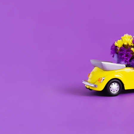 View of the back of the trunk of a bright yellow convertible car with a bouquet of flowers on a purple background. Concept holiday, delivery, art, background, transport.の写真素材