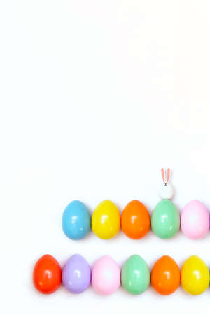 Top view of an Easter composition of painted eggs in bright juicy colors on a white background with a little rabbit. Holiday concept, flat layout, minimalismの写真素材