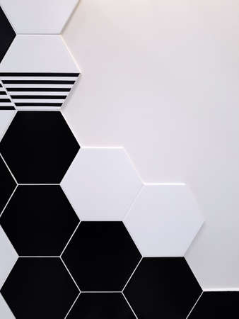 A background of black and white ceramic tiles in the shape of a hexagon that partially covers a white wall. Concept texture, backgroundの写真素材