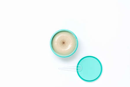 Top view of a bright turquoise jar with cosmetic cream next to which lies a lid with a spatula on a white background. The concept of beauty, medicine, facial and body skin care, hair careの写真素材
