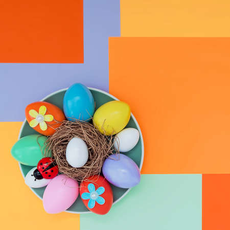 Bright background with an asymmetric geometric pattern in trendy colors with a composition of their Easter eggs, a ladybug and flowers lying on a plate. Concept background, holiday, easterの写真素材