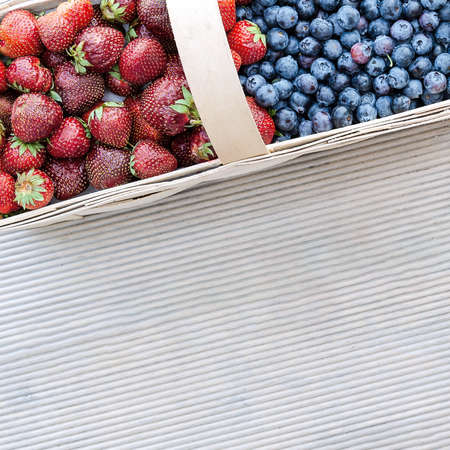 Fresh berries of strawberries and blueberries lie in a basket on the terrace boards on the veranda. Food concept, flat layout, gardening, summer, healthy eatingの写真素材