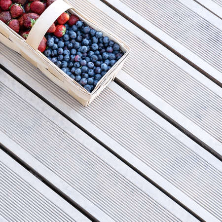 Fresh berries of strawberries and blueberries lie in a basket on the terrace boards on the veranda. Food concept, flat layout, gardening, summer, healthy eatingの写真素材