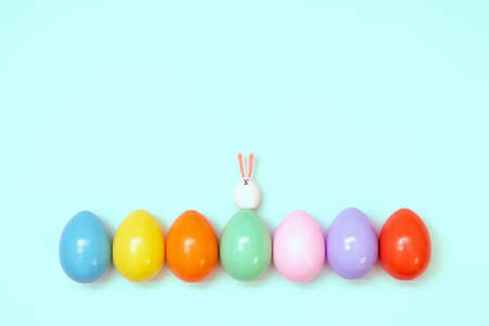 Top view of an Easter composition of painted eggs in bright juicy colors on a blue background with a little rabbit. Holiday concept, flat layout, minimalismの写真素材