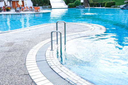 View of the pool in which a person is swimming on the background of a lawn with sunbeds, aqua slides and a street cafe. The concept of summer, vacation, spa, water park, travel, recovery, sportの写真素材