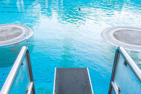 Top view close-up on a diving board against the background of a pool with blue water in which a person swims. The concept of summer, relaxation, spa, aqua park, sports, architectureの写真素材