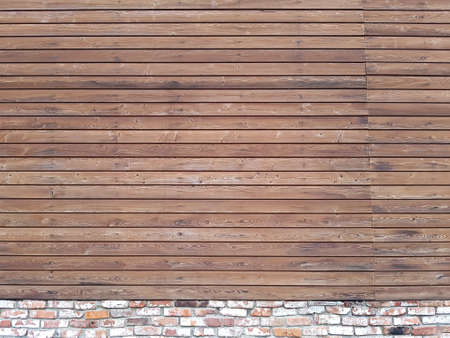 A solid wall of aged brown wooden planks with hammered nails located horizontally on a brick foundation. Concept for texture, background, interiorの写真素材