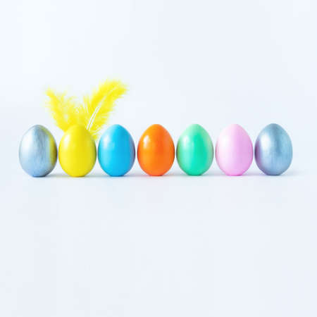 Top view of an easter composition of painted eggs in bright juicy colors on a white background with feather rabbit ears. Vacation concept, flat design, minimalism.の写真素材